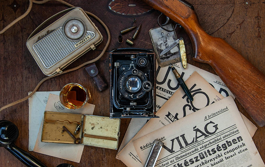 antique camera, vintage radio, old newspaper, brown wooden table, vintage items, black and silver camera, old-fashioned vibe, vintage collection, antique objects, retro items, vintage photography