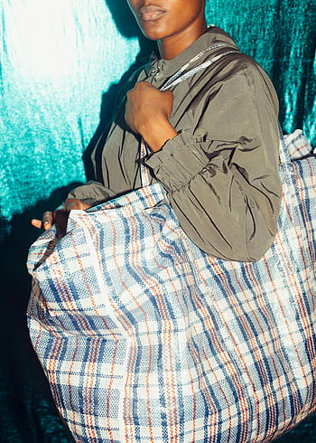 anonymous person, large plaid bag, blue wall, colorful setting, trendy fashion, checkered tote bag, stylish outfit, urban style, fashion photography, modern look, vibrant colors