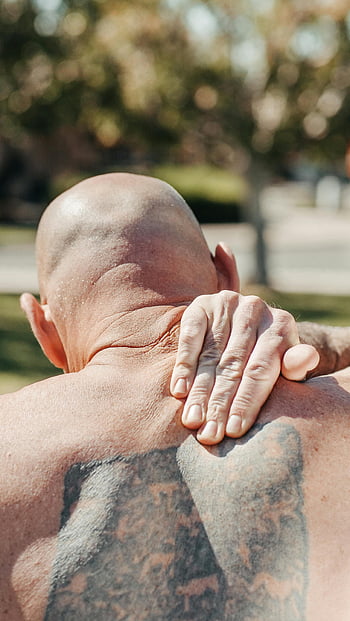 shoulder pain, bald man, tattoo, outdoor, pain relief, sore shoulder, man holding shoulder, outdoor setting, physical discomfort, male with tattoo, natural light