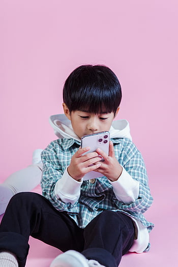 anak laki -laki etnis, memeriksa pesan, smartphone, Konektivitas Digital, gaya hidup modern, anak menggunakan telepon, Pengaturan dalam ruangan, pakaian kasual, latar belakang merah muda, Ekspresi terfokus, penggunaan teknologi