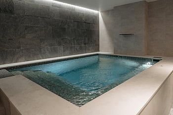 indoor spa pool, modern stone tile, relaxation, blue swimming pool, gray concrete wall, elegant interior, spa relaxation, indoor pool, stone tile interior, spa design, relaxation space