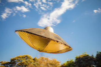 toy UFO, metallic UFO model, flying UFO, clear blue sky, close-up UFO, UFO in air, toy spacecraft, flying object, sky background, UFO photography, outdoor UFO shot
