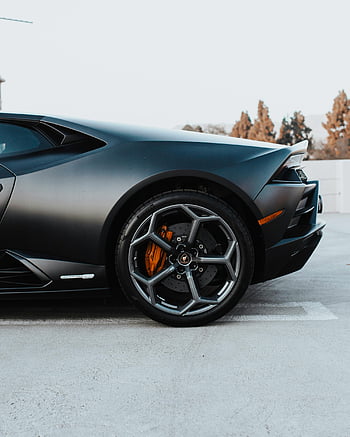 black sportscar, rear wheel, luxury car, side profile, concrete pavement, outdoor parking, high-performance vehicle, sleek design, sports car wheel, black rims, orange brake calipers
