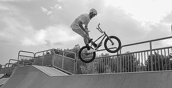 BMX bike tricks, ramp, skate park, cloudy sky, cyclist, BMX trick, outdoor, action sports, extreme sports, black and white, helmet