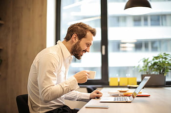 man, teacup, laptop, table, office, coffee, smiling, remote work, work environment, professional setting, indoor workspace