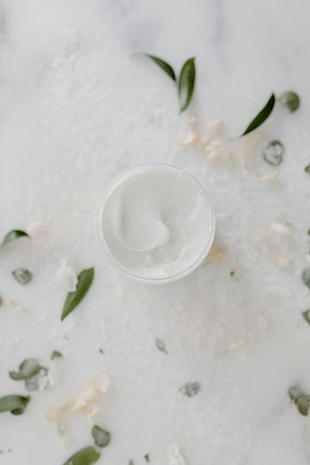 krim kosmetik putih, wadah bundar, toples krim perawatan kulit, daun-daun hijau, kelopak, permukaan putih, Pandangan atas, cantik alami, produk perawatan kulit, Estetika minimalis, Kemasan ramah lingkungan