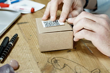hands packing box, QR code, online business services, brown cardboard box, close-up hands, packing process, business packaging, e-commerce packaging, shipping preparation, small business logistics, product packaging