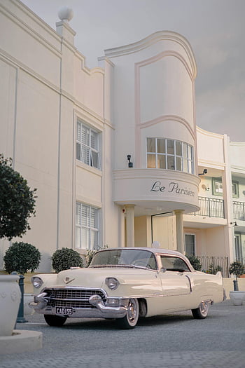 vintage car, classic white Cadillac, Art Deco building, vintage style, overcast sky, Le Parisien, classic car, vintage architecture, white building, outdoor scene, retro vehicle