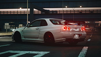 white Nissan coupe, parked under bridge, night scene, luxury sports car, performance vehicle, urban setting, rear view, city lights, sleek design, modern car, street parking