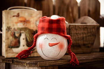 snowman glass figurine, brown wooden surface, red checkered hat, cozy winter decor, charming snowman, festive decoration, holiday ornament, winter theme, decorative item, seasonal decor, indoor decoration