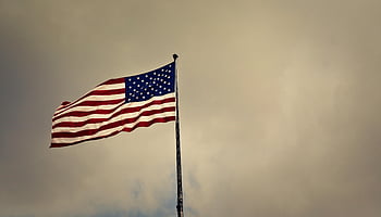 American flag, cloudy skies, US flag, waving flag, freedom symbol, patriotism, cloudy weather, flag pole, outdoor scene, wind blowing, cloudy day