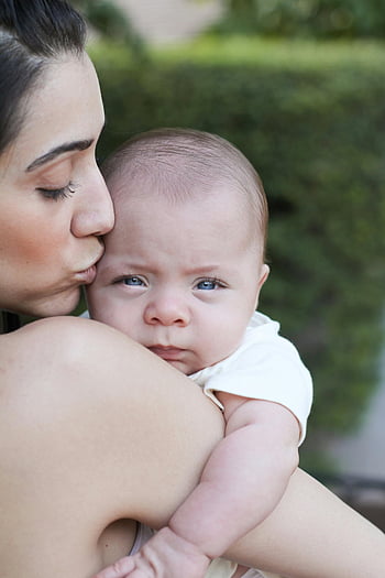 Madre besando bebé, cerca de la foto, Momento cariñoso, ajuste al aire libre, madre e hijo, expresión de bebé, momento tierno, vínculo familiar, maternidad, fotografía de bebé, fotografía al aire libre