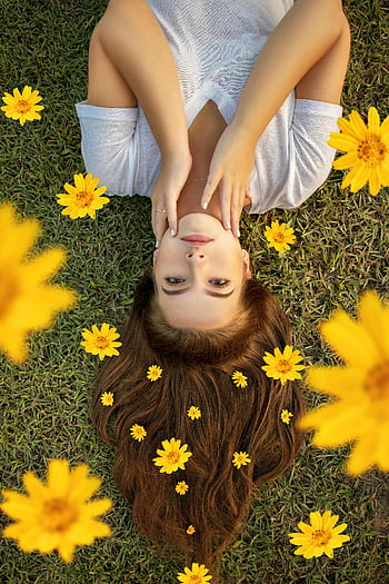 upside down photo, woman portrait, lying on grass, yellow flowers, hair decoration, outdoor photography, nature scene, floral arrangement, casual outfit, serene moment, artistic composition