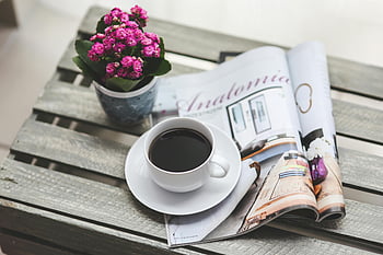 coffee, magazine, pink flowers, wooden table, relaxing scene, coffee cup, open magazine, floral arrangement, cozy setting, outdoor table, reading time