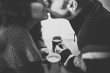 grayscale photo, couple kissing, romantic kiss, coffee, cozy setting, black and white, couple, romance, coffee cups, intimate moment, black-and-white photography