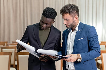 businessmen, black suit, blue suit, conversation, holding documents, reviewing contracts, business documents, indoor setting, professional meeting, two businessmen, formal attire