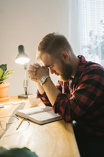 vousatý muž, modlí se, kostkovaná košile, zavřené oči, lavice, bible, měkké vnitřní osvětlení, Vnitřní modlitba, náboženský okamžik, studijní stůl, osobní reflexe