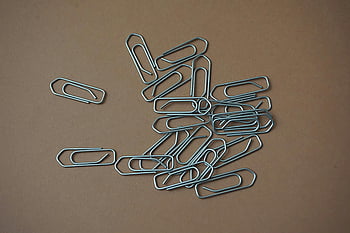 metal paper clips, brown table, office supplies, gray paper clip, scattered paper clips, brown surface, metal clips, desk accessories, stationery items, office organization, paperclip collection