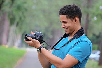 sort DSLR-kamera til mænd, smilende mand, afslappet foto, grøn park, udendørs fotografering, Kamerabrug, parkens indstilling, mand med kamera, fotografisk hobby, naturfotografering, udendørs aktivitet