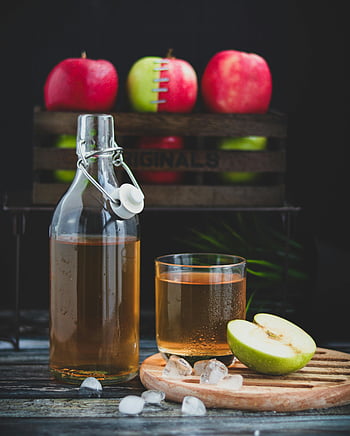 glass bottle, brown liquid, glass of cold drink, chilled apple cider, fresh apples, ice cubes, refreshing drink, wooden crate, sliced apple, ice, wooden table