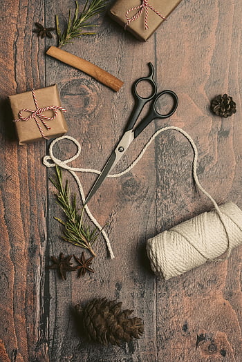 Pakowanie prezentów świątecznych DIY, elementy naturalne, powierzchnia drewniana, szpula nici, nożyczki, płaski układ, szyszki sosnowe, laska cynamonu, anyż gwiazdkowaty, rozmaryn, pudełka na prezenty