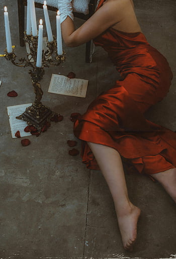 woman, red silk dress, concrete floor, chandelier, candlelight, romance, dramatic pose, vintage candelabra, rose petals, open book, evocative scene