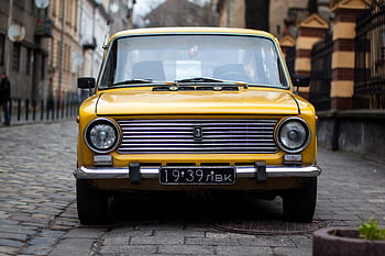 vintage yellow car, cobblestone street, Lviv Ukraine, front view, parked car, vintage vehicle, urban scene, classic car, yellow car, European city, street view