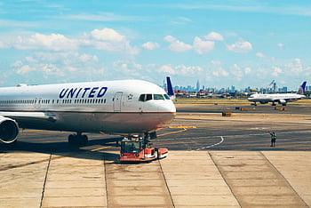 white airplane, man in green vest, Newark Airport, aircraft on runway, city skyline, United Airlines, airport tarmac, airport worker, commercial airplane, airport operations, runway scene