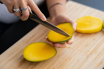 mango, sliced fruit, cutting board, fresh tropical fruit, hands slicing, close-up, yellow fruit, fruit preparation, mango slices, tropical fruit, kitchen cutting