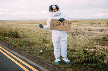 astronaut, hitchhiking, spacesuit, rural road, cardboard Earth sign, travel, adventure, roadside, space travel, cosplay, cardboard sign