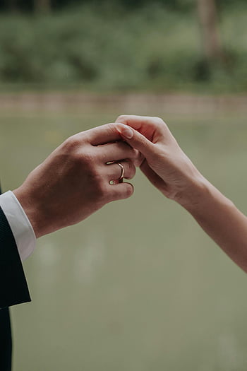 snubní prsten, pár drží za ruce, Láska a spojení, detailní fotografie, venkovní nastavení, romantický okamžik, zásnubní prsten, Svatební pár, ruku v ruce, romantické gesto, Venkovní milostná scéna
