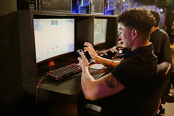 man in black shirt, using smartphone, sitting by gaming computer, young man gaming, smartphone gaming, PC setup, mechanical keyboard, indoors, gaming computer, indoor gaming