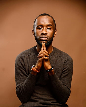 thoughtful man, brown knit sweater, matching background, dramatic pose, holding hands, gray long sleeve shirt, portrait photography, studio shot, professional photography, male model, contemplative expression