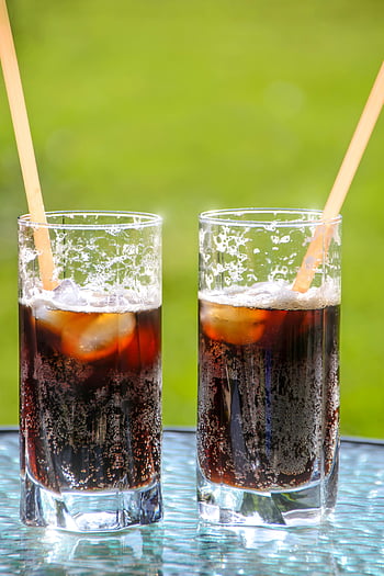two glasses, iced cola, straws, summer refreshment, cold drinks, beverage, ice cubes, glass cups, outdoor setting, refreshing drinks, soda