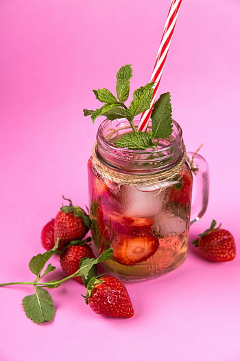 strawberry mint iced drink, mason jar, pink background, strawberries, mint leaves, clear glass jar, iced drink, red and white straw, vibrant drink, refreshing beverage, summer drink