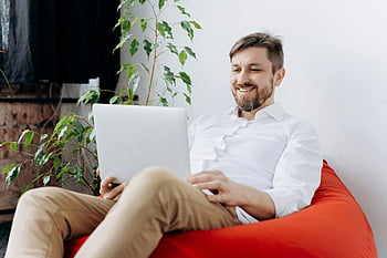 happy man, laptop, red bean bag chair, smiling, casual workspace, modern workspace, man using laptop, relaxed setting, indoor environment, green plant, comfortable seating