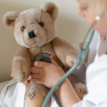 child playing doctor, teddy bear, stethoscope, playful interaction, stuffed toy, close-up shot, doctor's check-up, child's play, teddy bear check-up, child with stethoscope, teddy bear examination