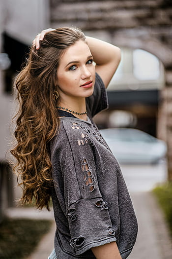 Žena na sobě šedé šaty, Stylová mladá žena, dlouhé vlasy, představuje sebevědomě, příležitostná elegance, venkovní portrét, sebevědomá pozice, neformální móda, Šedé oblečení, dlouhé kudrnaté vlasy, pouliční styl