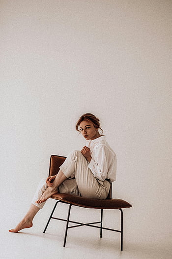 donna alla moda, seduto sulla sedia, impostazione in studio, Studio minimalista, giovane donna, posando con grazia, camicia bianca, pantaloni beige, Sedia moderna, a piedi nudi, fotografia al coperto
