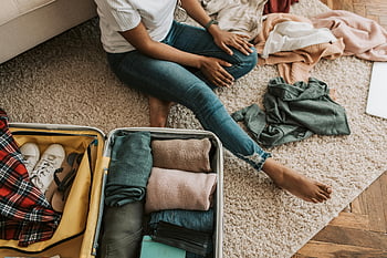 woman packing suitcase, organizing clothes, preparing for trip, sitting on floor, open suitcase, travel preparation, packing clothes, suitcase contents, casual outfit, indoor setting, carpet floor