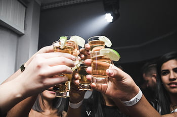 people doing cheers, friends raising tequila shots, lime, lively indoor bar, social gathering, group celebration, party atmosphere, tequila shots with lime, indoor bar setting, friends toasting, group cheers