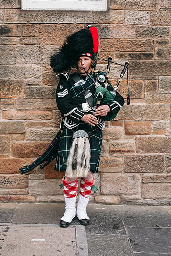 Scottish bagpiper, Edinburgh streets, classic attire, kilt, traditional music, Scottish culture, street performer, bagpipes, Scottish heritage, traditional clothing, stone wall background