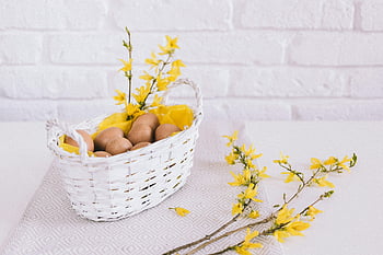 uova marroni, cestino bianco, fiori gialli, cestino a tema primaverile, Tovaglia testurizzata, muro di mattoni, decorazione di Pasqua, arredamento primaverile, cesto di vimini, composizione floreale, uova di Pasqua