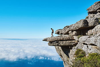 Homme en débardeur gris, bord de la falaise, mer de nuages, ciel bleu vif, personne seule, falaise dramatique, aventure en plein air, vue panoramique, Paysage naturel, photographie d'aventure, photographie de voyage