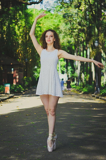 woman dancing outdoor, young ballerina, sunlit path, lush park, graceful pose, ballet dancer, outdoor dance, park setting, ballet shoes, natural light, dance photography