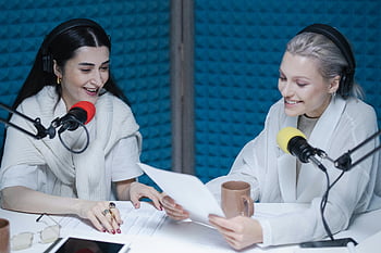 women in studio, podcast recording, professional studio, two women, lively podcast, studio setting, microphones, headphones, paper documents, coffee mug, studio equipment