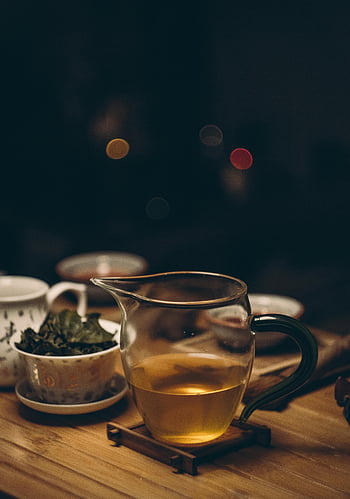 clear glass cup, brown wooden table, tea setup, soft bokeh, warm inviting, wooden table, tea pitcher, tea leaves, cozy atmosphere, tea time, bokeh background