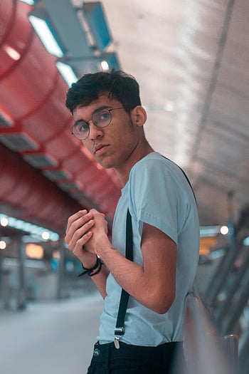 men's white crew neck shirt, fashionable young man, glasses, suspenders, urban indoor setting, casual pose, modern fashion, stylish outfit, indoor fashion photography, casual attire, urban style