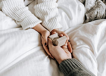 návrh, zásnubní prsten, ruce páru, Útulné nastavení, intimní okamžik, Láska a odhodlání, kroužek, anonymní člověk, přítelkyně, romantické gesto, bílé ložní prádlo