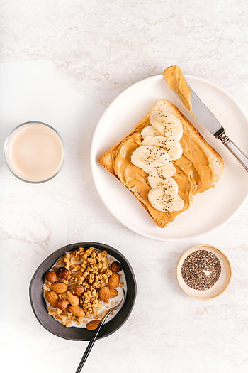 toast alla banana al burro di arachidi, noccioline, semi di chia, superficie di marmo, vista dall'alto verso il basso, piatto in ceramica bianca, Coltello in acciaio inossidabile, prima colazione, pasto salutare, ciotola di muesli, latte di mandorla